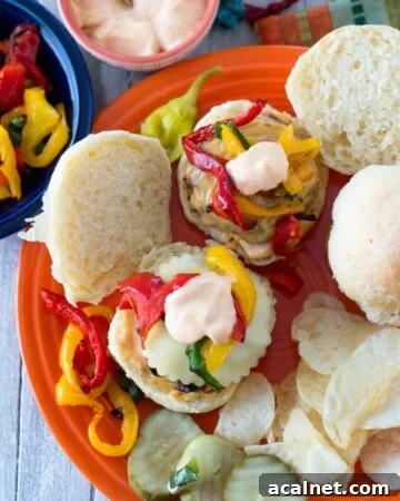 A dinner plate with 2 chicken sliders, sliced pickles, and chips.