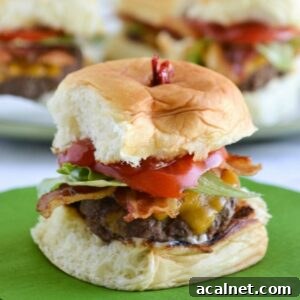 A stuffed bacon cheeseburger slider with toppings on a plate.