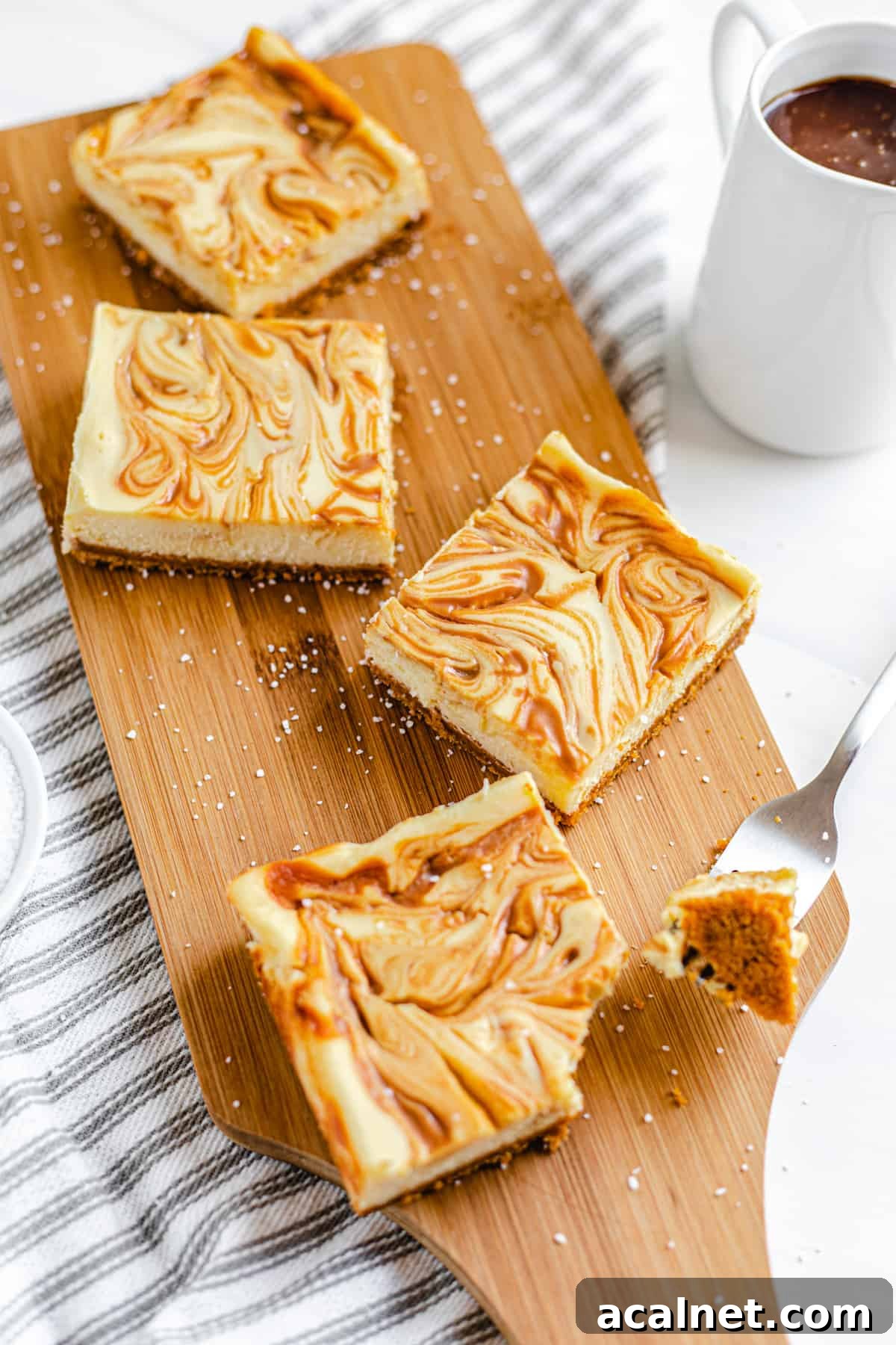 cheesecake bars on a wooden board with pitcher of caramel next to it and bite taken out of the front bar