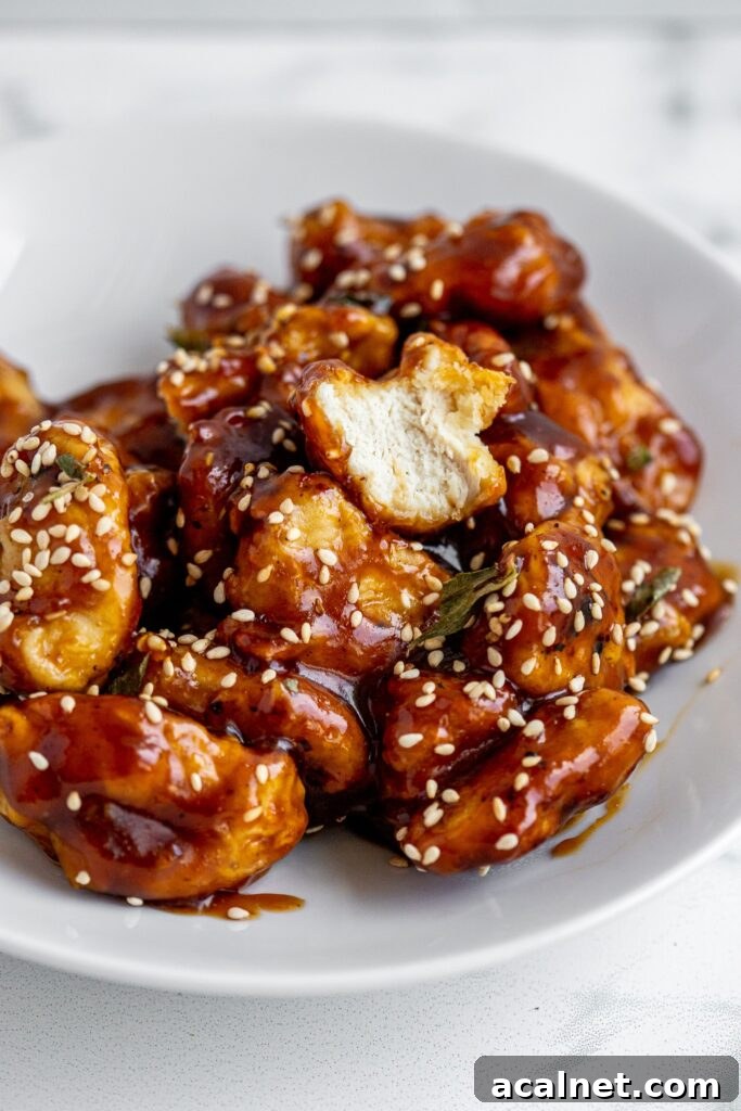Crispy Air Fryer Sesame Chicken Bites — 62g Protein Per Serving 2 Bite shot of crispy air fryer sesame chicken bites stacked on white plate with sesame seeds and green onions — 62g protein