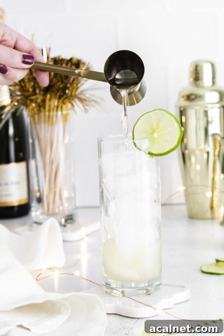 Pouring a shot from a jigger into a sparkling margarita cocktail.