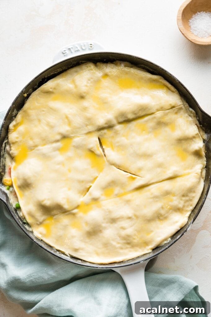 Puff pastry cut and shaped to fit on top of a skillet pot pie, brushed with egg wash and with three air vents cut in.