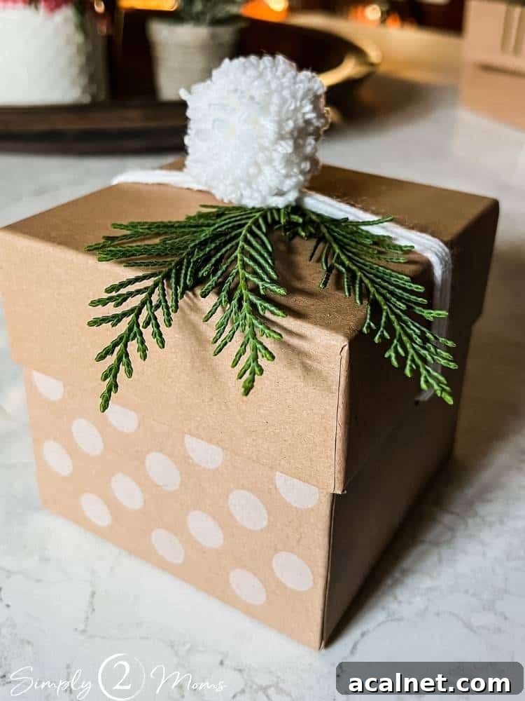 Kraft box with white yarn wrapped and a small pompom with greenery