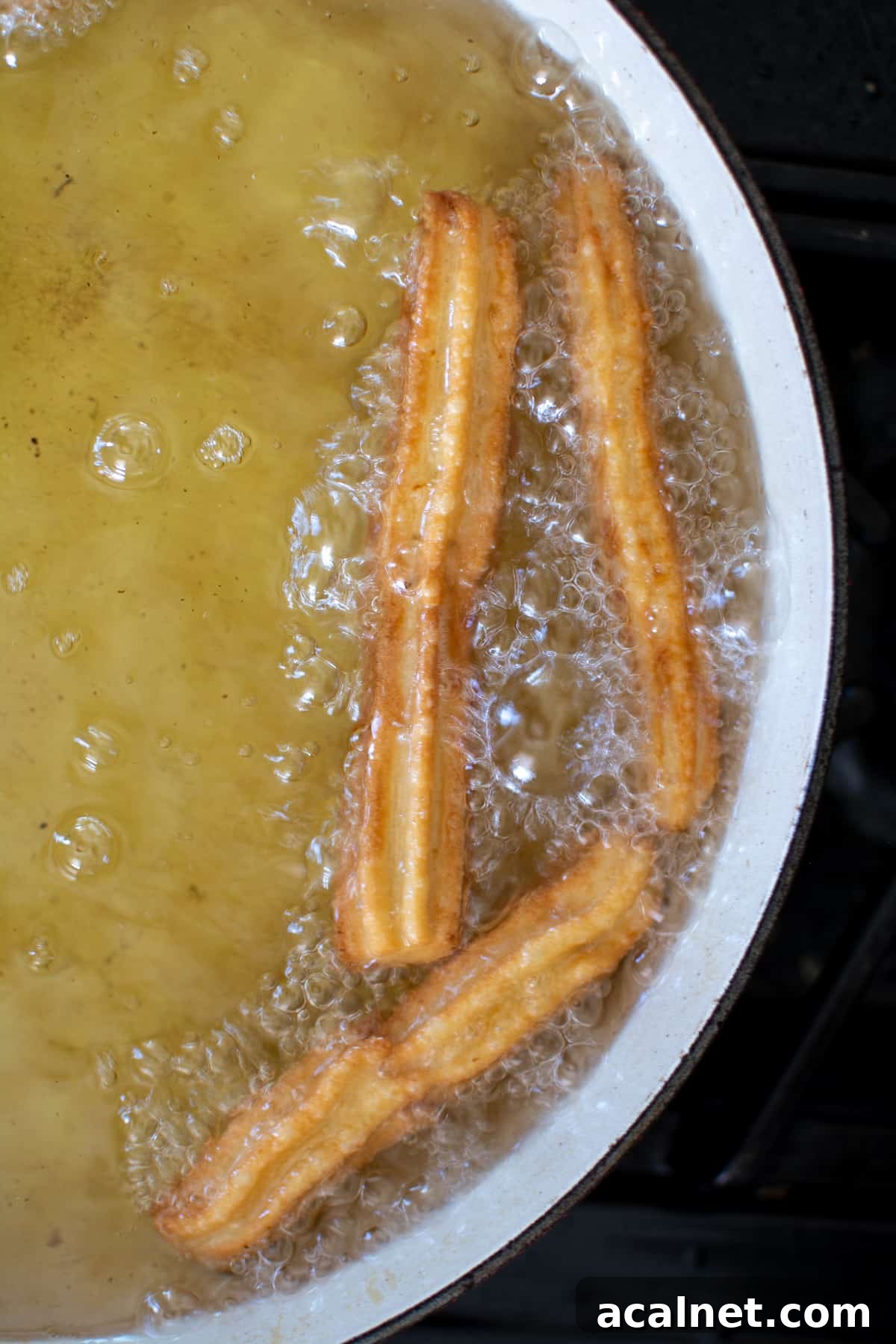 Churros frying in oil in a wide pot on the stove.