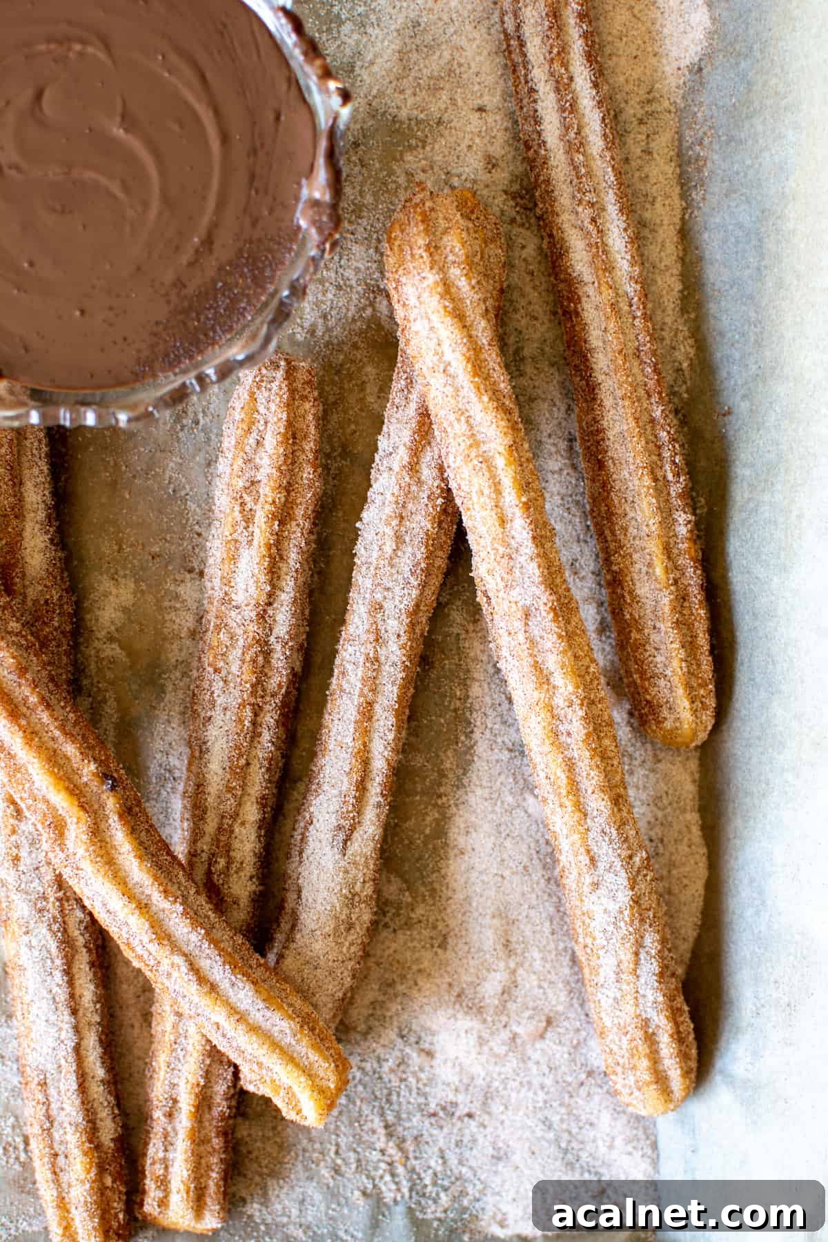 Several churros covered in cinnamon and sugar with a glass bowl of chocolate sauce next to them.
