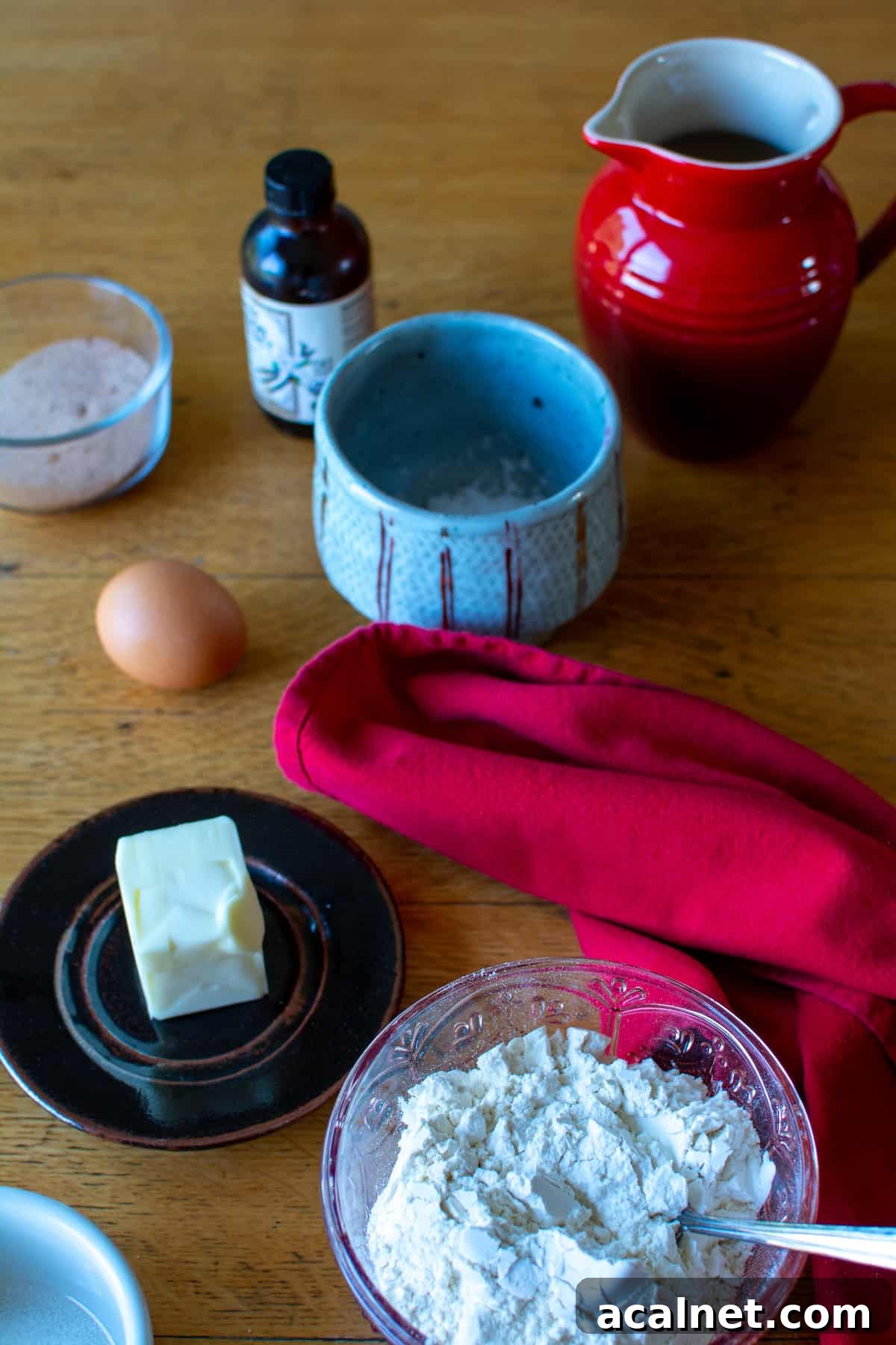Ingredients to make churros sitting on a wood table including flour, butter, egg, salt, water, cinnamon-sugar, and vanilla extract.
