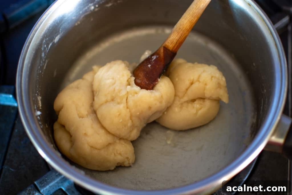 A dough in a saucepan being stirred with a wood spoon