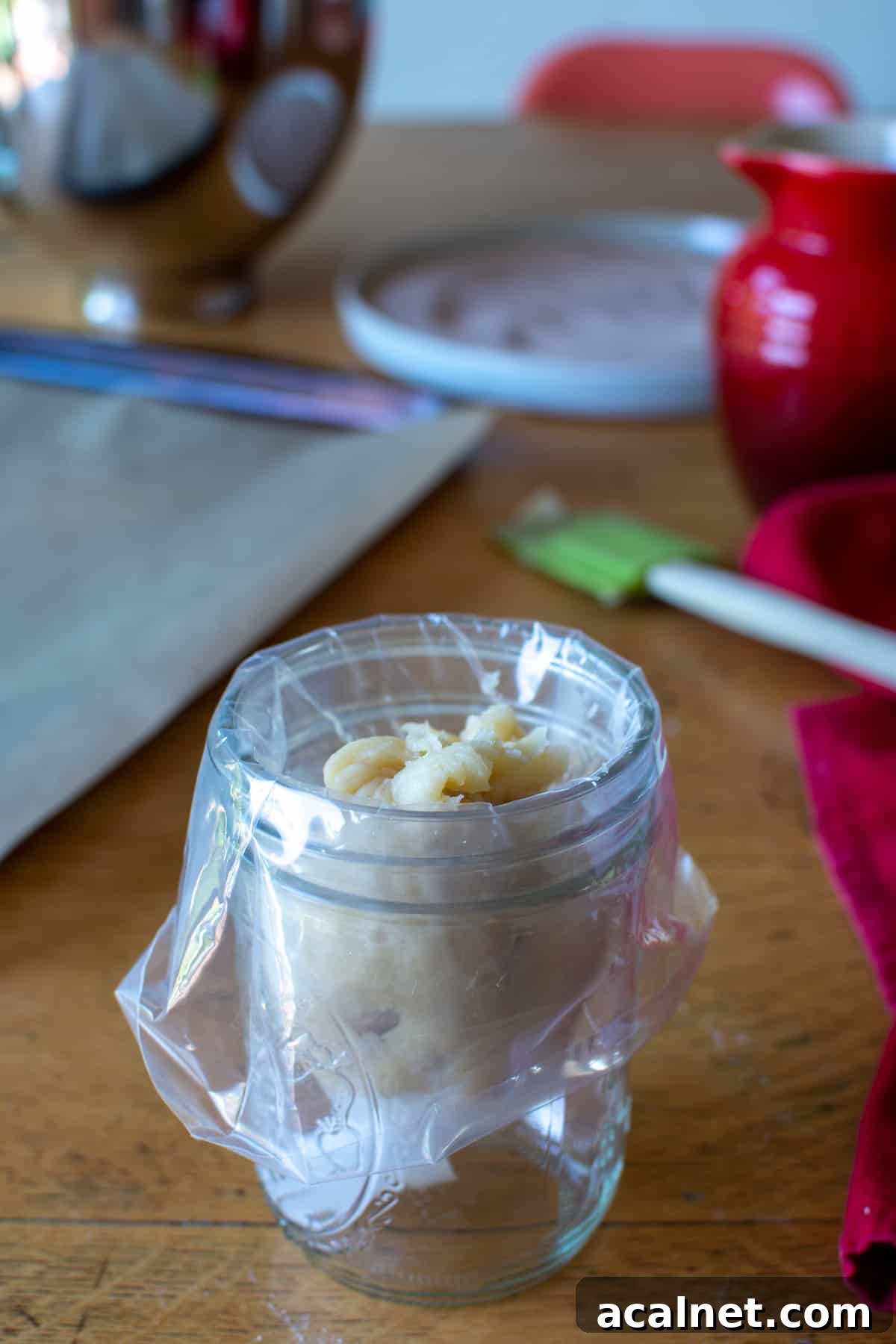 Churro dough in a piping bag that is placed inside a Mason jar. The jar in on a wood table with a baking sheet near by.