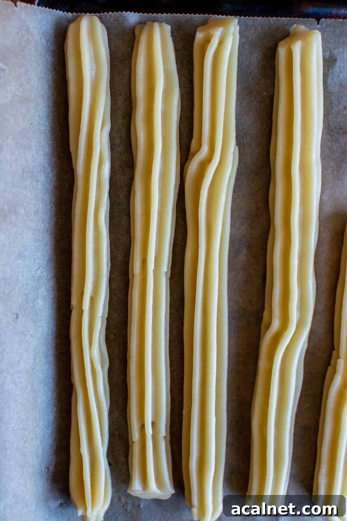 Churros waiting to be fried on a parchment-lined baking sheet.