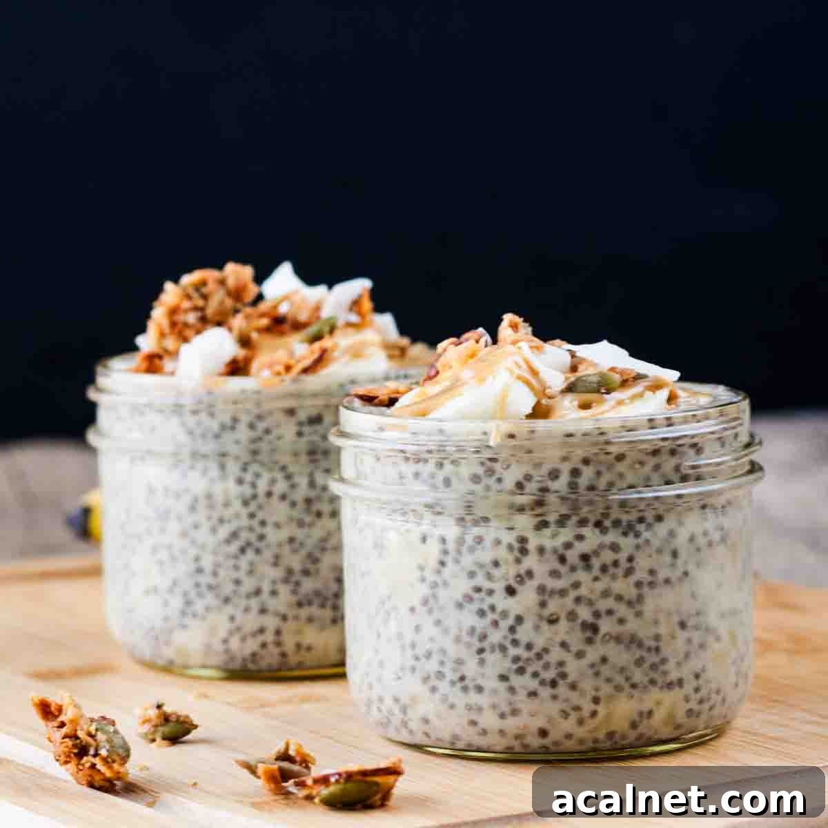 Creamy Banana Chia Seed Pudding Recipe 2 Two jars of banana chia pudding on a wooden board, topped with banana and granola.