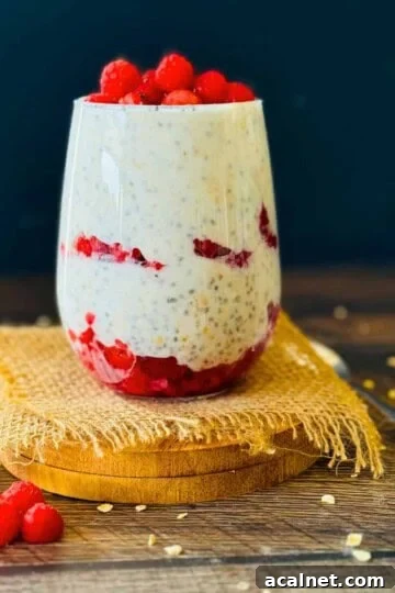 A small glass filled with raspberry overnight oats and topped with fresh raspberries.