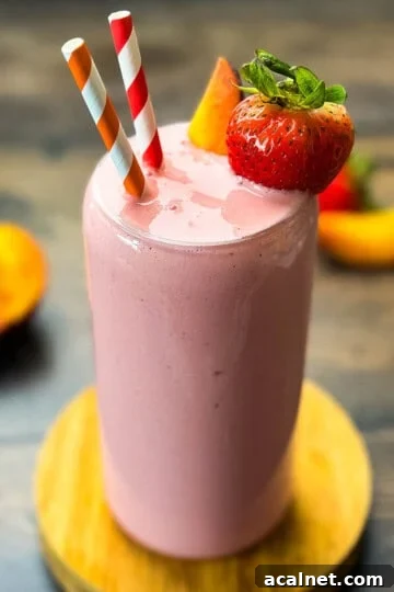Strawberry peach smoothie in a tall glass garnished with fresh strawberry slices and peaches.