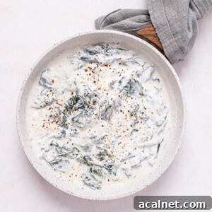 Garlic Parmesan Creamed Spinach Recipe 2 Overhead view of Easy Creamy Spinach in a white ceramic skillet with wooden handle and gray towel wrapped around the handle