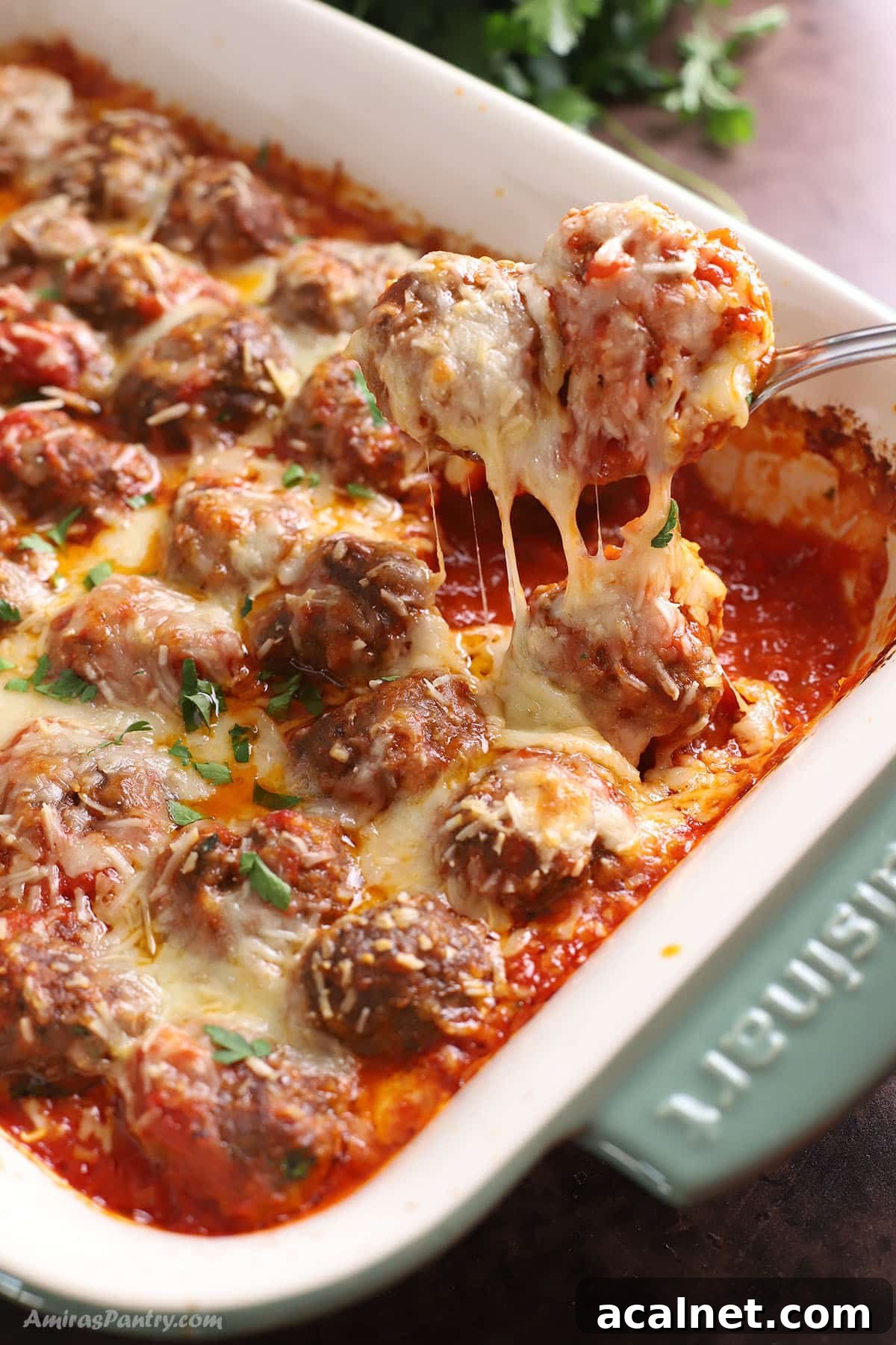 A green ceramic casserole with baked meatballs topped with melty cheese.