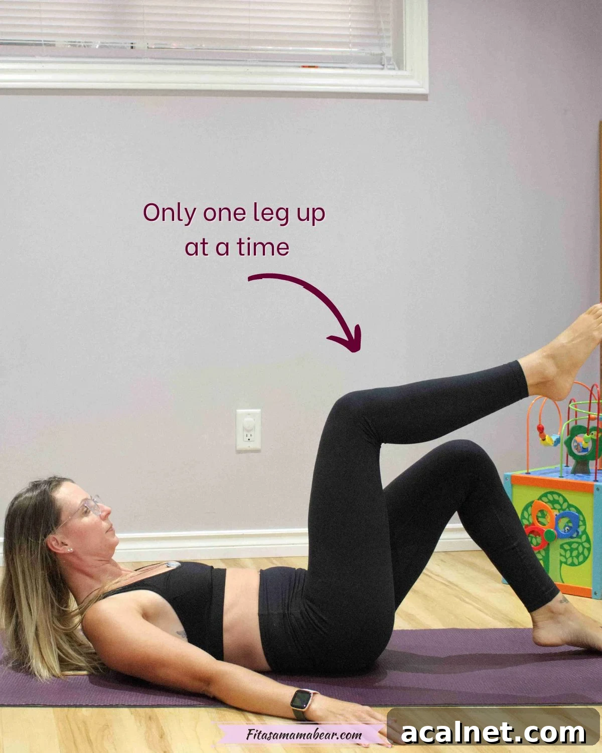 Woman in black sports bra and pants laying on the ground raising her legs one at a time