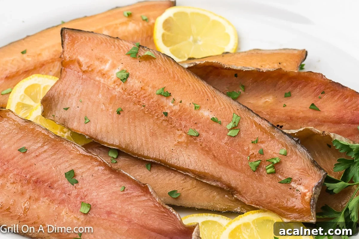 Smoked salmon fillets on a white platter with lemon slices and fresh herbs.