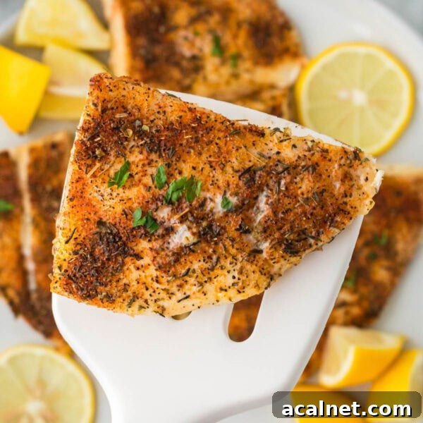 Juicy, seasoned grilled fish fillet with lemon wedges on a white serving spatula.