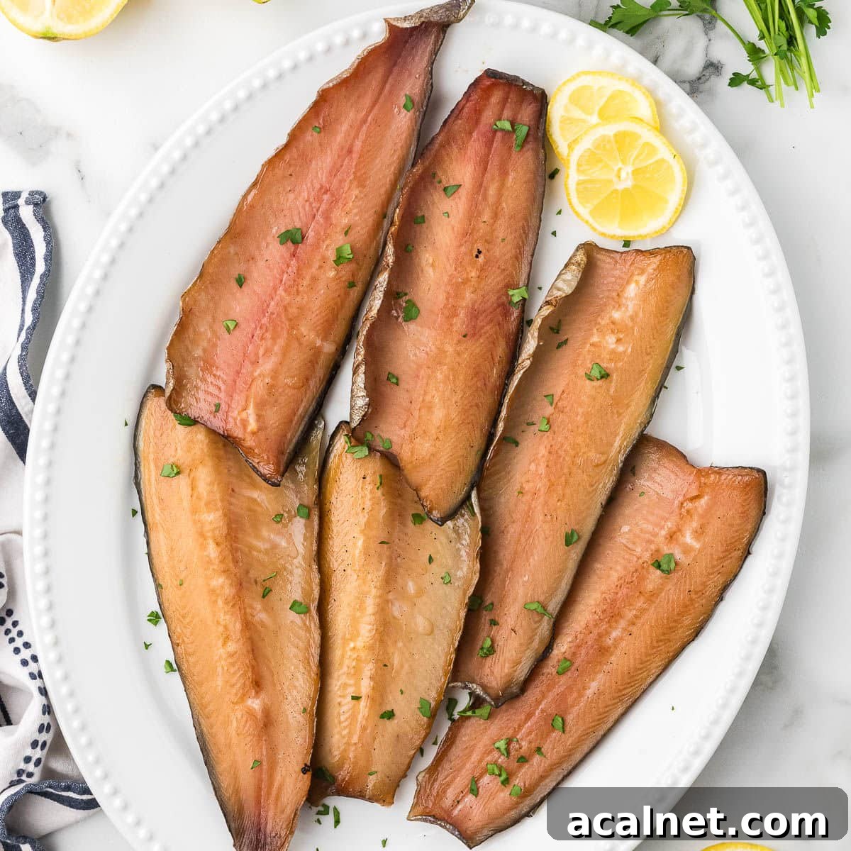 Smoked salmon fillets on a white platter with lemon slices and fresh herbs.