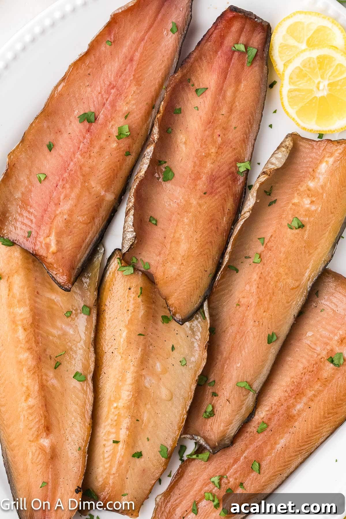 Smoked salmon fillets on a white platter with lemon slices and fresh herbs.