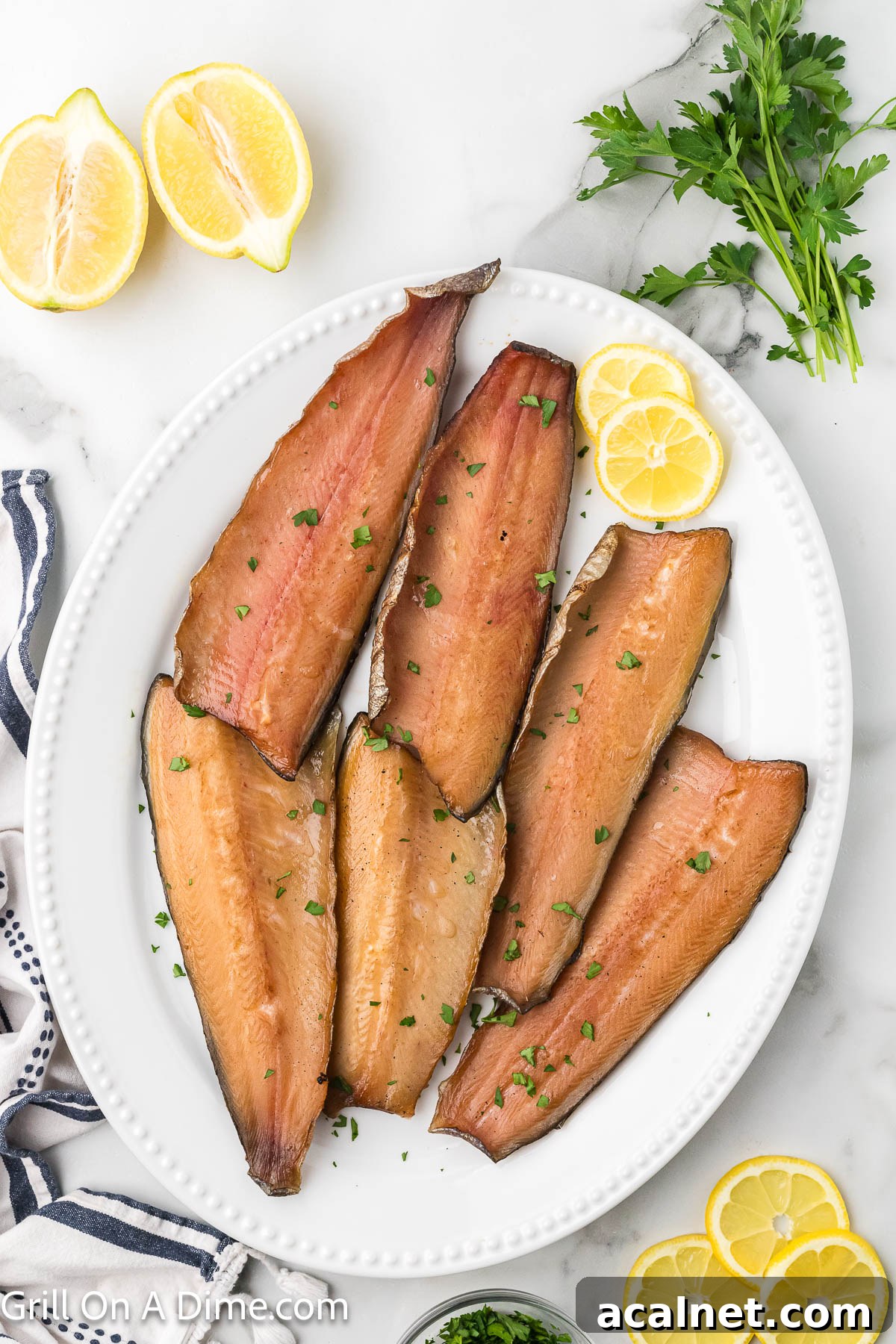 Smoked salmon fillets on a white platter with lemon slices and fresh herbs.