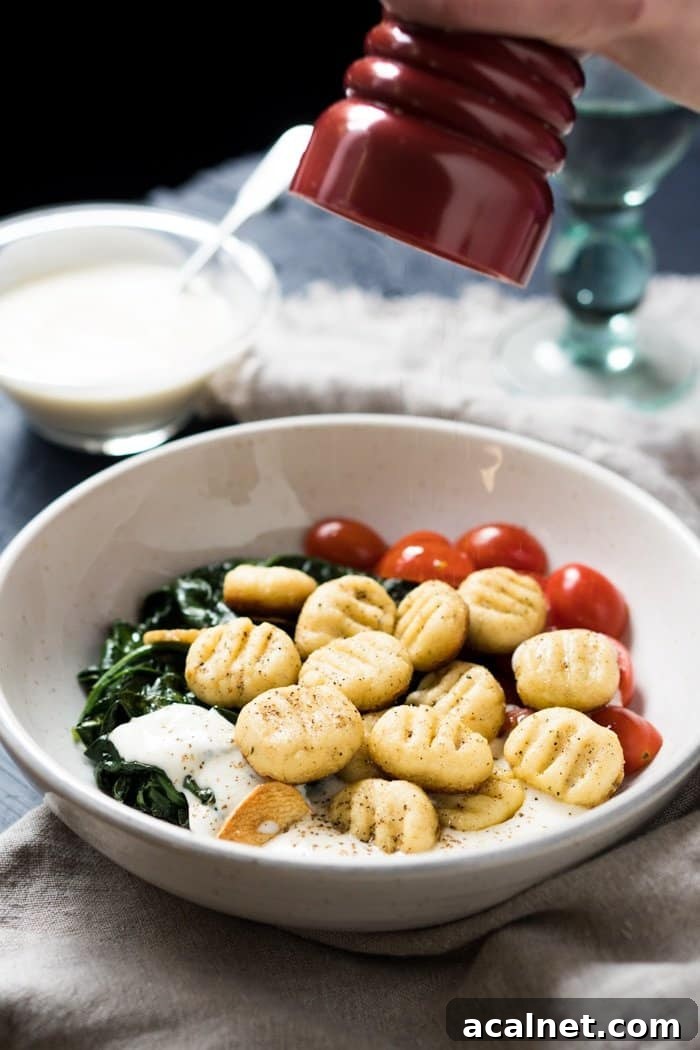 Freshly grinding black pepper onto a plate of keto ricotta gnocchi