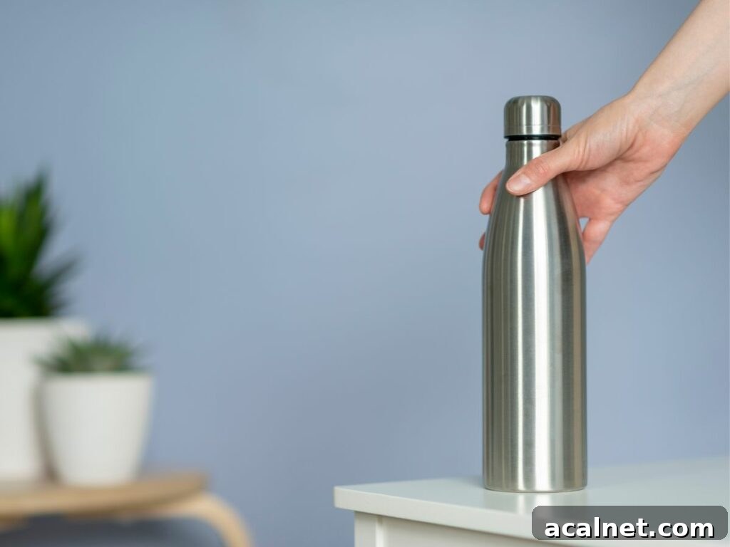 A person holding a stainless steel water bottle on a table.