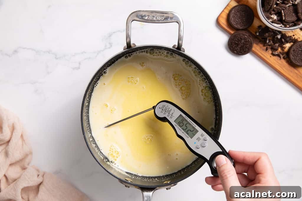 A saucepan with combined egg yolks, sugar and milk with scraped vanilla bean. A thermometer is in it to read the temperature.