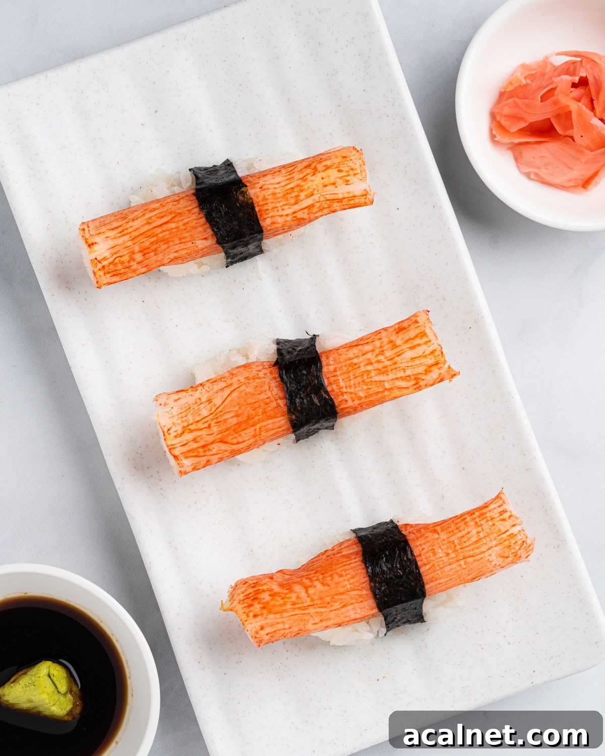 Top down view of Kanikama nigiri sushi on a white plate with a side of soy sauce, wasabi and pickled ginger.