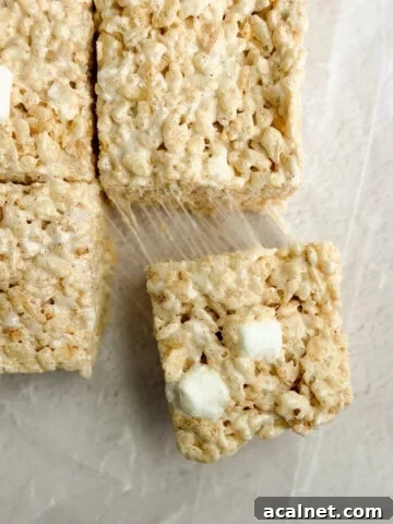 a close up of brown butter rice krispie treats with a marshmallow being pulled and stretched.