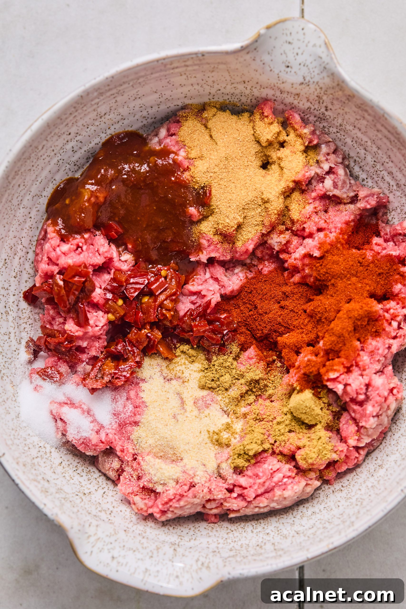 Smoky Chipotle Beef Burgers with Creamy Aioli 6 A large white mixing bowl filled with ground beef, chopped chipotle peppers, chipotle sauce, smoked paprika, garlic powder, onion powder and salt ready to be mixed into burger patties