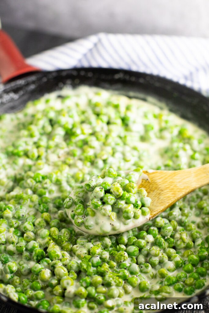 A wooden spoon taking a scoop of creamed peas out of a cast iron skillet.