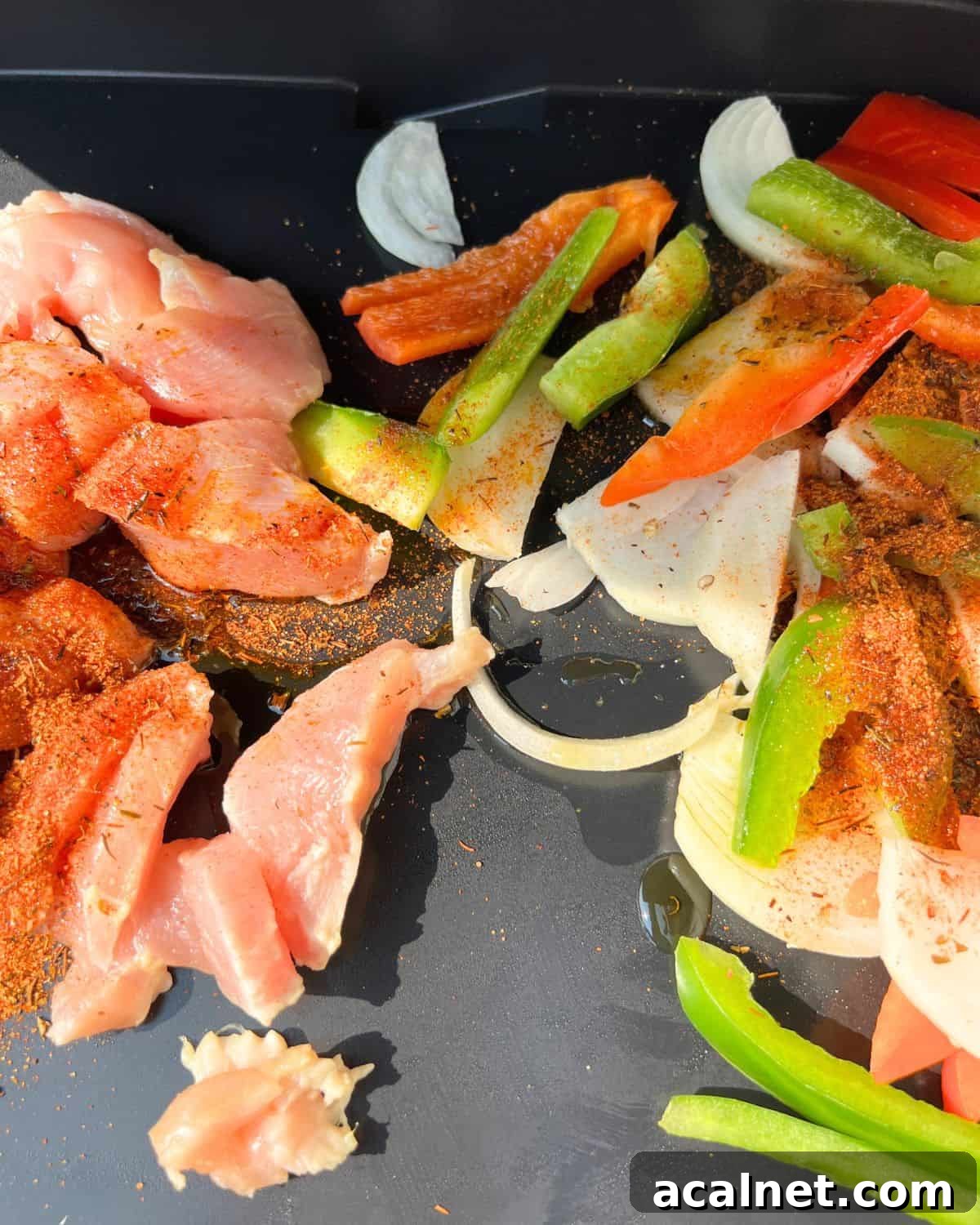 Uncooked seasoned chicken and vegetables on a griddle.
