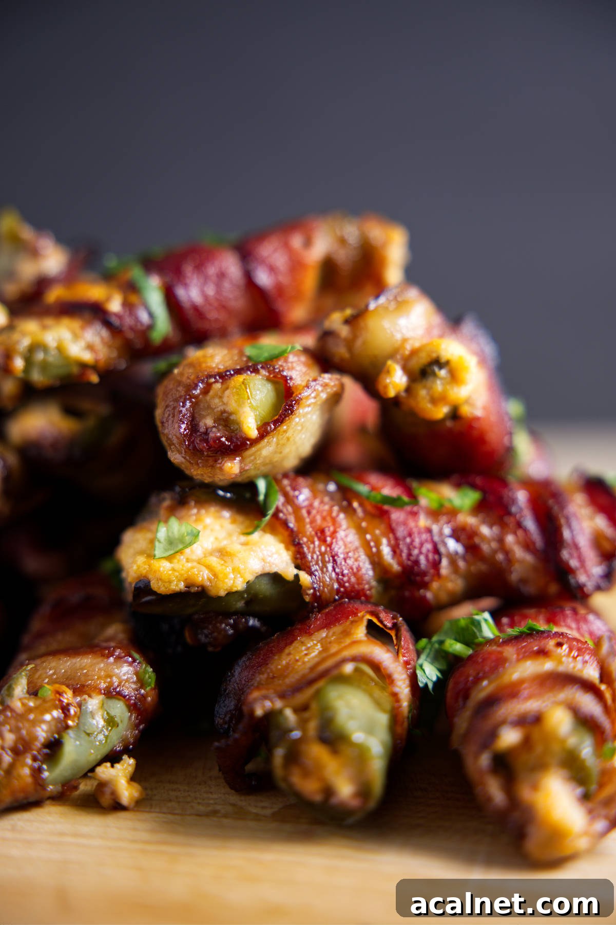 Large pile of bacon wrapped jalapeño poppers with cheese oozing out.