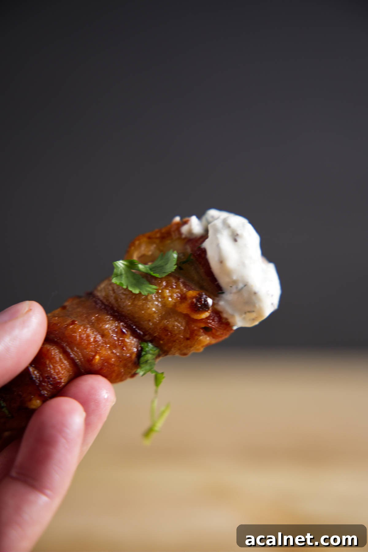 Single bacon wrapped jalapeño popper dipped in blue cheese dressing held in hand.