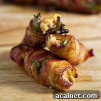 Stacked jalapeño poppers on a cutting board, and these are wrapped in crispy bacon!