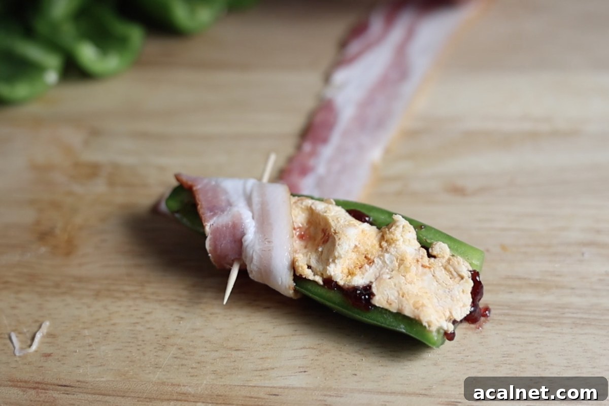 Wrapping stuffed jalapeno in a slice of bacon.