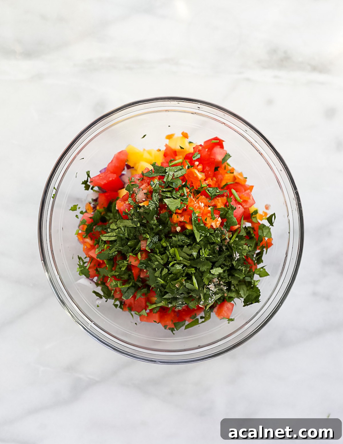 A clear glass bowl filled with unmixed mango salsa.