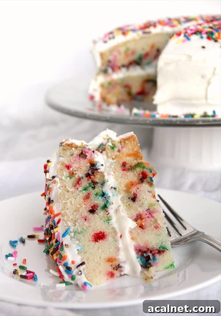 Slice of homemade funfetti cake on a white plate with a whole cake in the background.