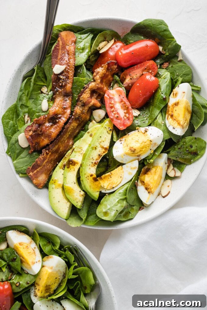 Spinach salad with bacon and eggs in a white bowl.
