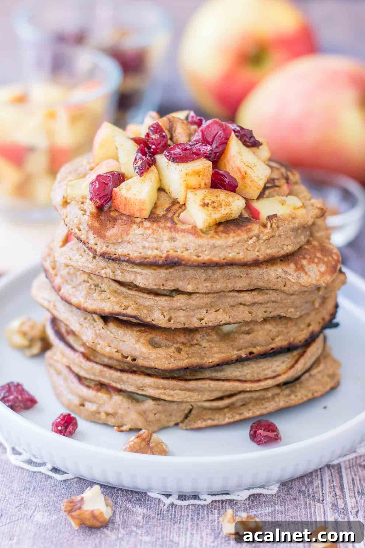 Apple Oatmeal Pancakes stacked on a plate topped with diced apples and cranberries