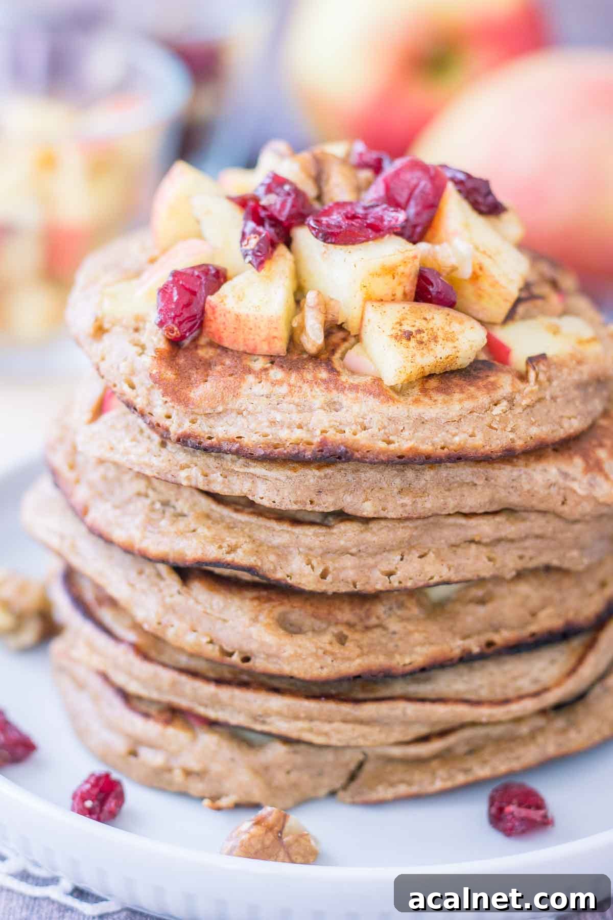 Apple Oatmeal Pancakes stacked on a plate topped with diced apples and cranberries