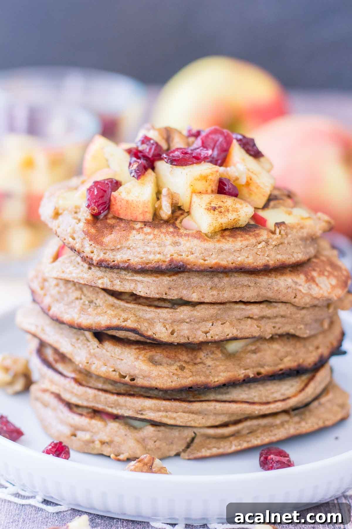 Apple Oatmeal Pancakes stacked on a plate topped with diced apples and cranberries