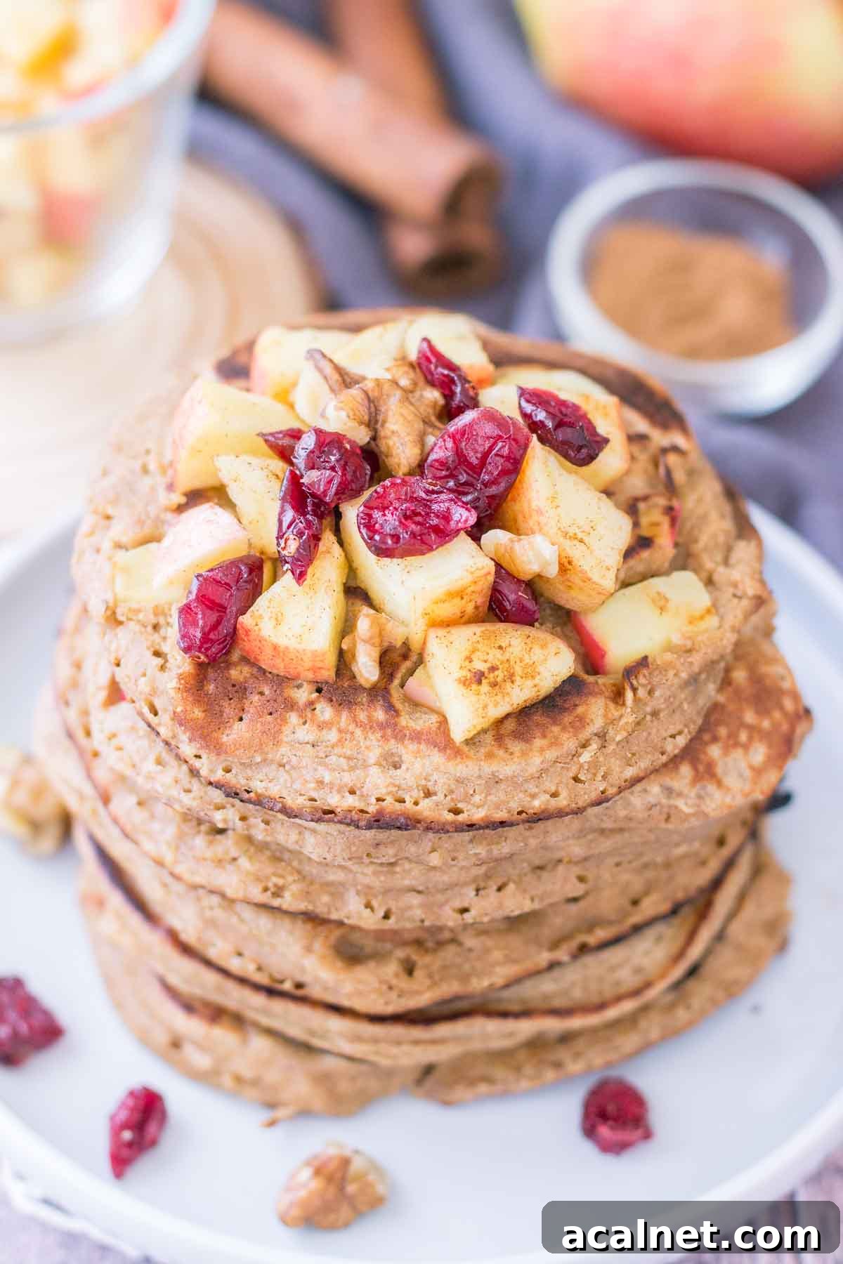 Apple Oatmeal Pancakes stacked on a plate topped with diced apples and cranberries