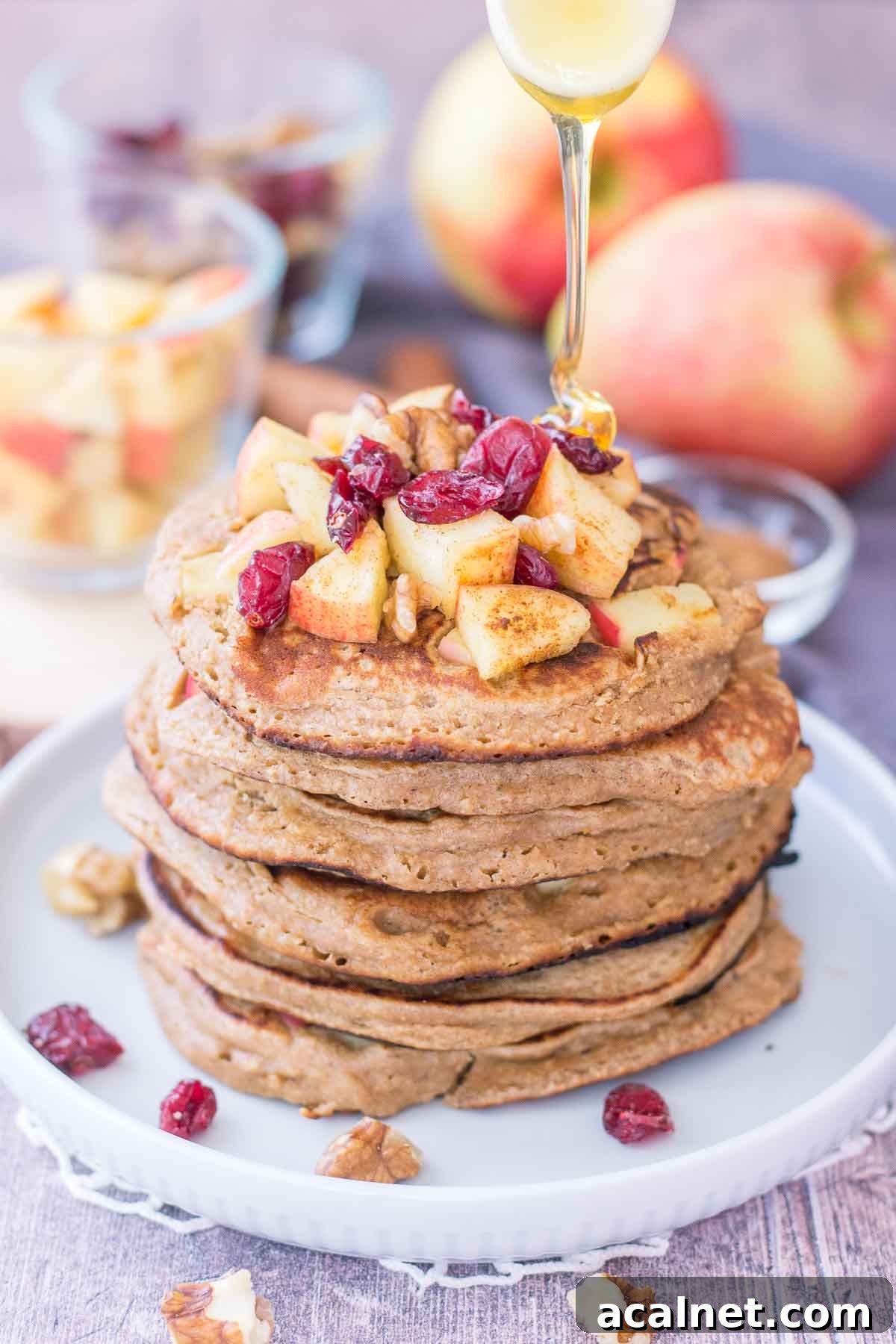 Apple Oatmeal Pancakes stacked on a plate topped with diced apples and cranberries