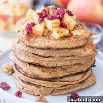 Apple Oatmeal Pancakes stacked on a plate topped with diced apples and cranberries