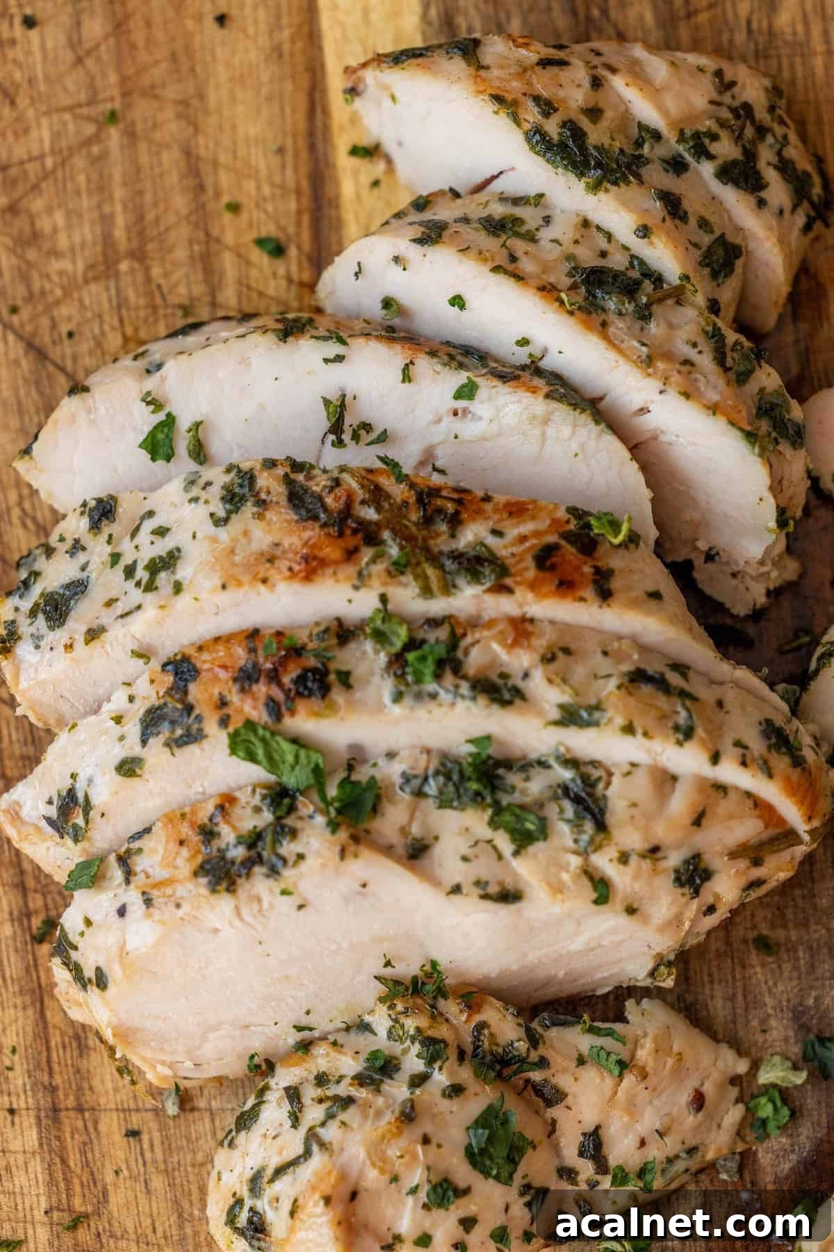Sliced herb-seasoned cooked chicken breast on a wooden cutting board, perfect inspiration for an easy turkey recipe or swapping with flavorful baked turkey tenderloin.