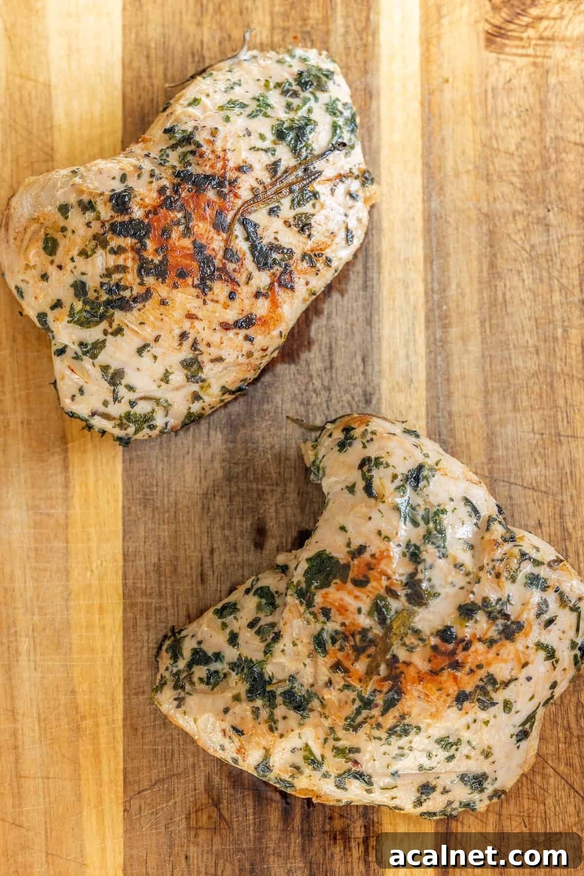 Two cooked, herb-seasoned turkey tenderloin pieces rest on a wooden cutting board—an easy turkey recipe perfect for any meal.