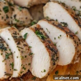 Sliced cooked chicken breast garnished with chopped herbs on a wooden cutting board—a presentation perfect for showcasing an Easy Turkey Recipe or Baked Turkey Tenderloin as well.