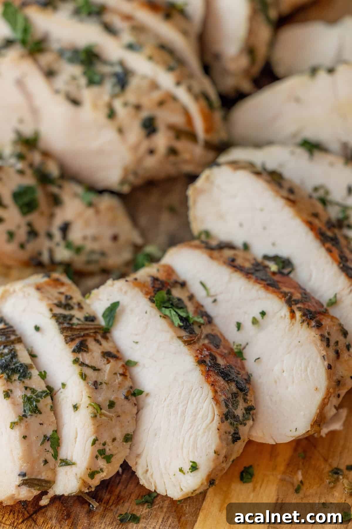 Sliced, cooked chicken breast with herbs on a wooden cutting board—perfect inspiration for an easy turkey recipe like baked turkey tenderloin.
