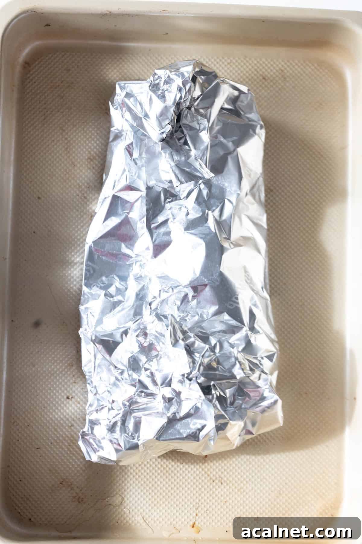 A baking tray with a rectangular object wrapped in crumpled aluminum foil, ready for an easy turkey recipe like baked turkey tenderloin.